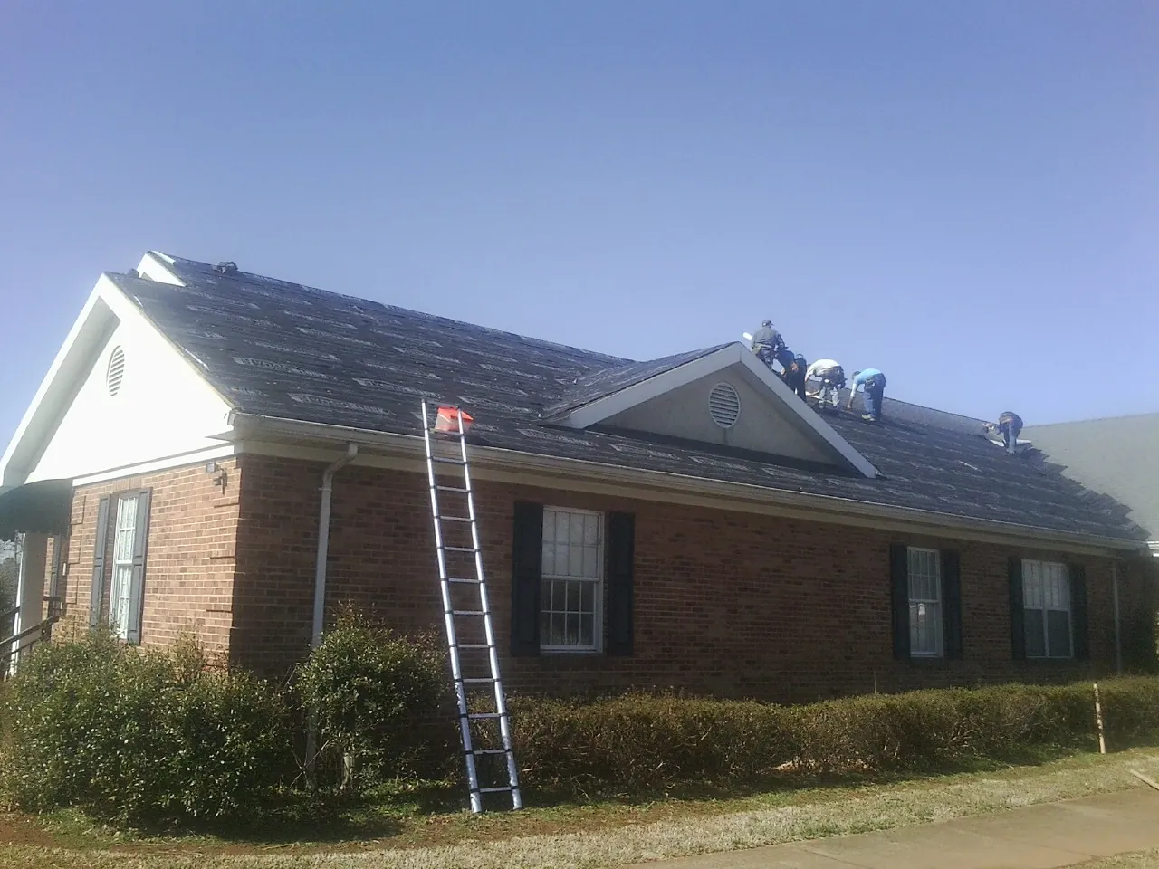 Crew tearing shingles off a brick ranch roof with a ladder set — Emergency Roof Repair work by our crew in Canal Fulton
