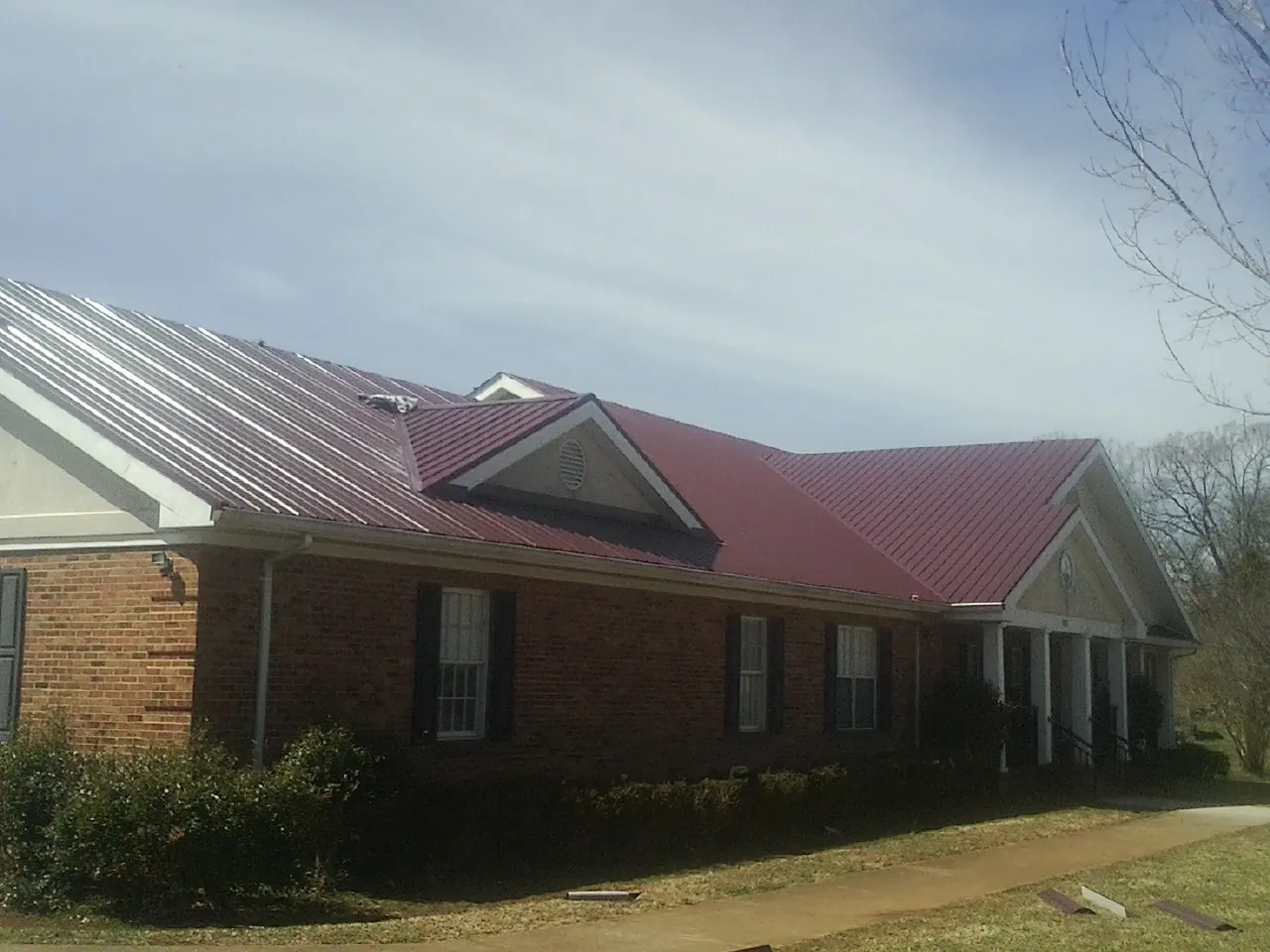 Red metal roof with gabled entries on a long brick building, from a Hail Damage Roof Repair job in Canal Fulton
