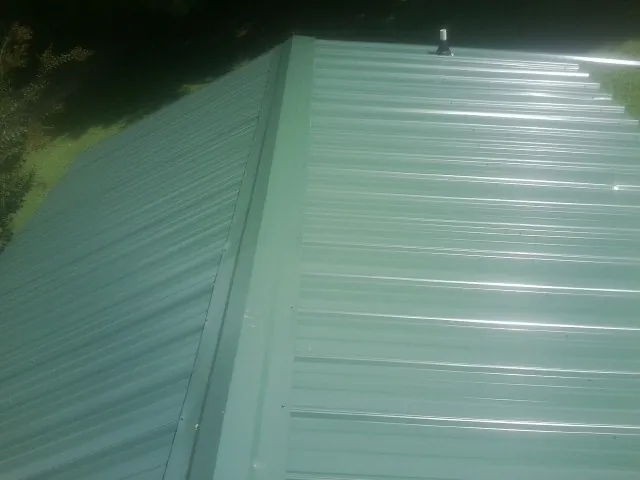 New green metal panels meeting at the ridge of a roof — Flat Roof Repair work by our crew in Canal Fulton
