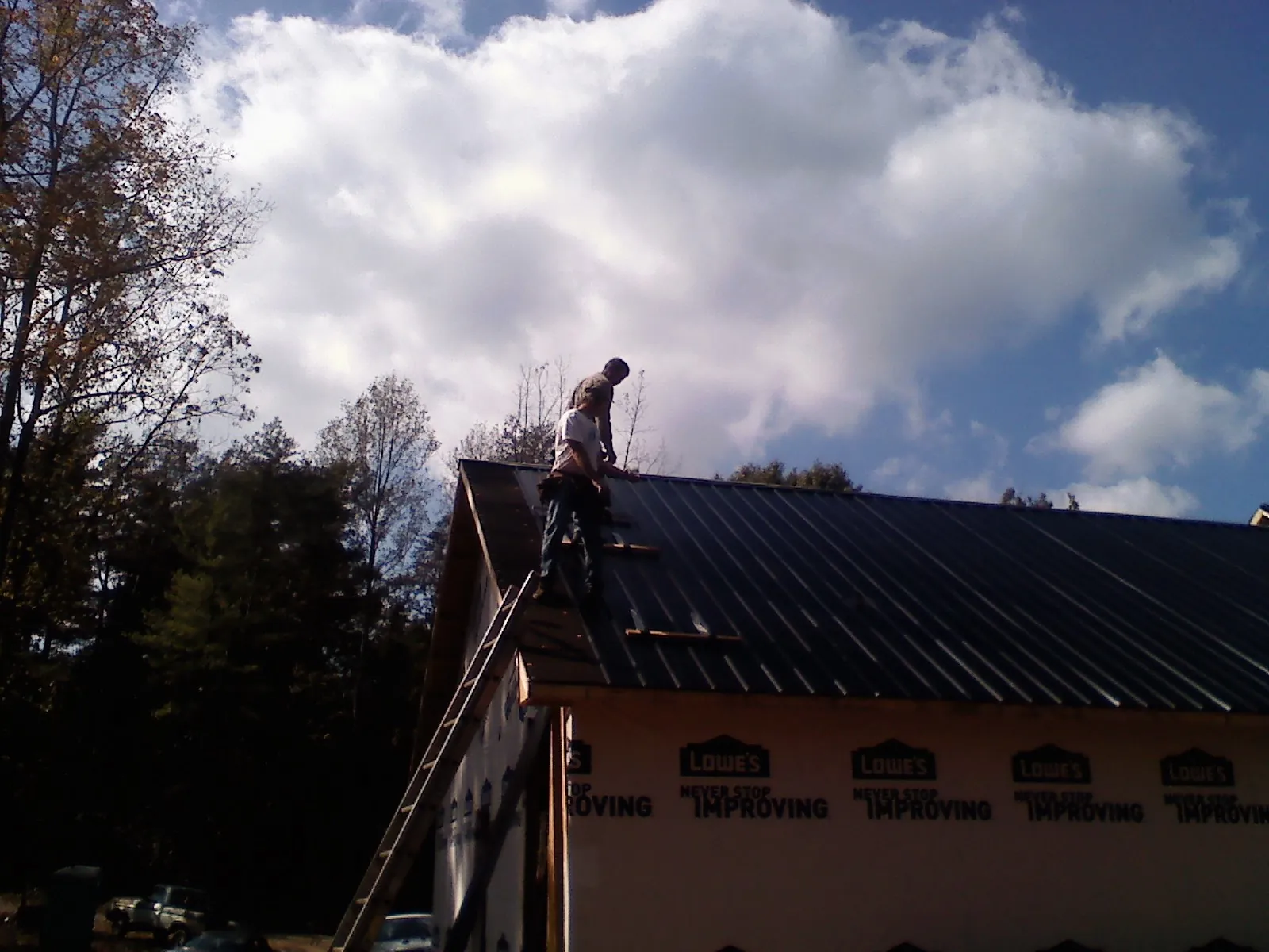Roofer fastening dark metal panels high against a cloudy sky, from a Roof Inspection job in Canal Fulton