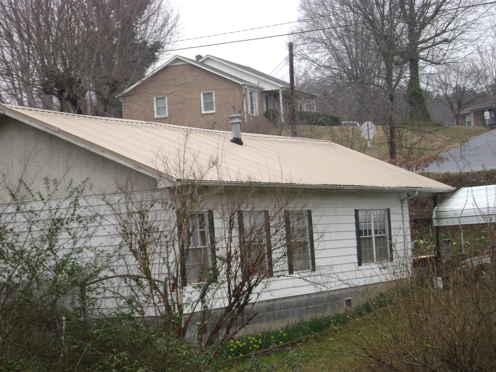 Tan metal roof on a white sided house set into a hillside — Commercial Roofing by Roofing Brothers in Canal Fulton